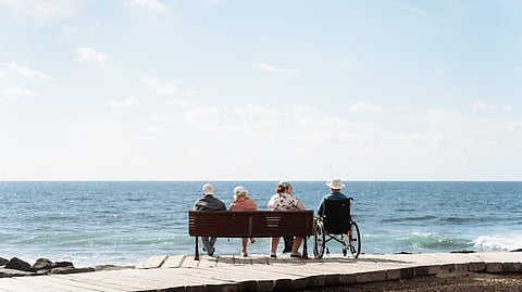 Three adults sitting on a bench near a beach and another on a wheelchair.