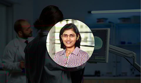 A woman wearing a lab coat studies a computer screen, focused on her work in a scientific environment.