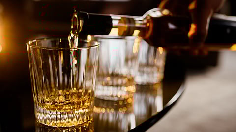 an illustration shows that a person filling the glass of alcohol drink from the bottle.