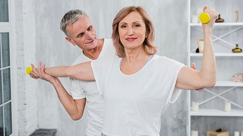 A senior couple are exercising together by lifting dumbbells at home.