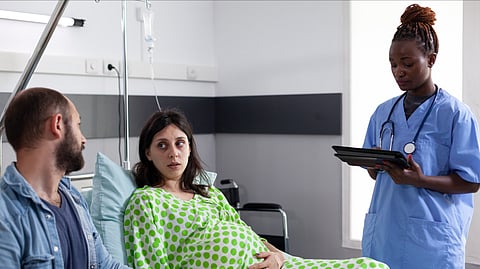 A pregnant couple is receiving medical advice from a nurse in a hospital ward.