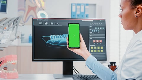 A woman dentist demonstrates a computer with a green screen, highlighting AI's role in oral cancer detection.