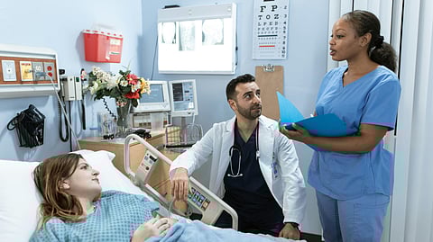 A nurse is explaining something to a patient on a bed while a doctor is also listening.