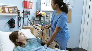 A nurse is checking the BP of a female patient lying on a bed.
