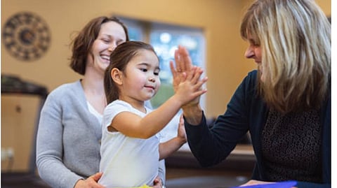 A young girl is high fiving another older lady with her mother nearby.