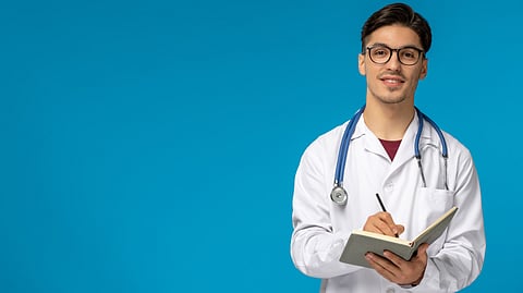 A Male Medical student in a white apron and stethoscope taking notes
