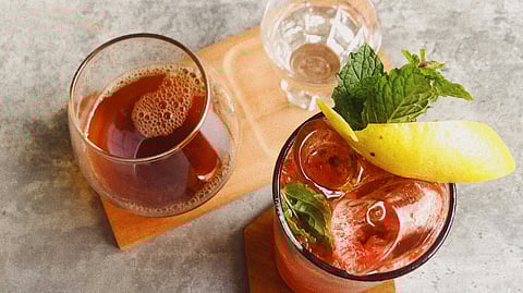 Two cups- one filled with some herbs and lemon and other with some fizzy drink on a wooden borad.