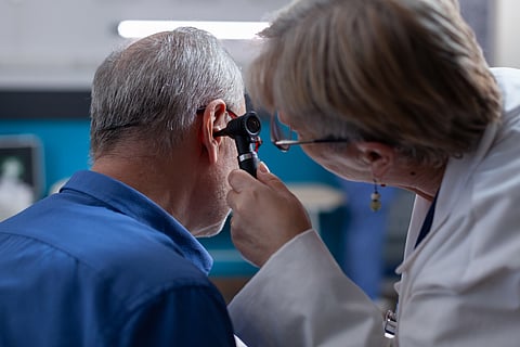 Woman doctor holding otoscope to do ear consultation for old man at medical appointment.