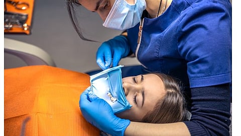 An oral surgeon is doing a dental procedure on a patient on dental chair.