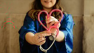 A woman in a graduation gown proudly holds a heart-shaped stethoscope, symbolizing her achievement in the medical field.
