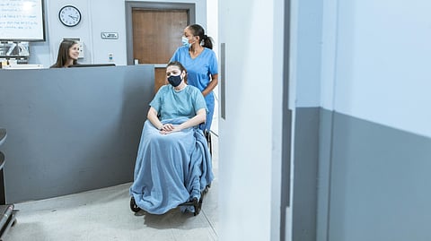 A nurse assisting a patient in a wheelchair in a hospital corridor.