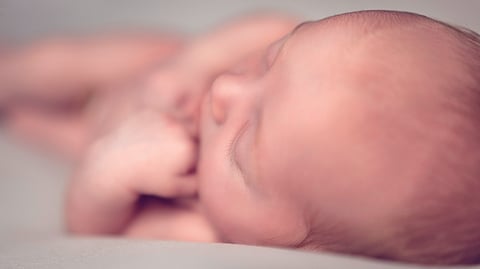 A newborn baby is peacefully lying on its side, wrapped in a soft blanket, with a serene expression on its face.