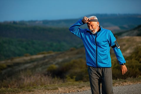 Senior man with a blue jacket wiping his forehead tired after a trek.