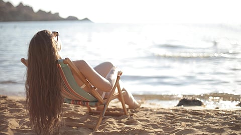 A woman is sitting in an easy chair on a beach tanning.