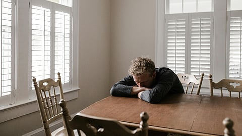 A man sitting on a chair leaning his head on a dining table alone.