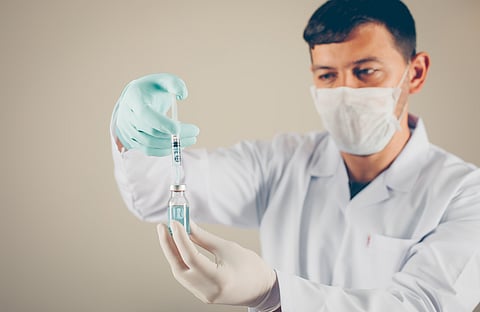A laboratory technician with gloves and mask unfilling the syringe into a vial.