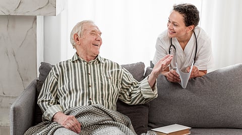 An elderly man talking to a health professional sitting on a couch.