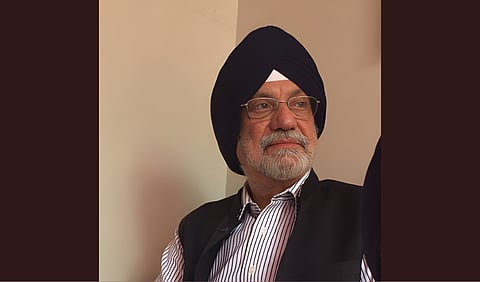 Dr. Meharban Singh wearing a black turban and white shirt with a black coat.