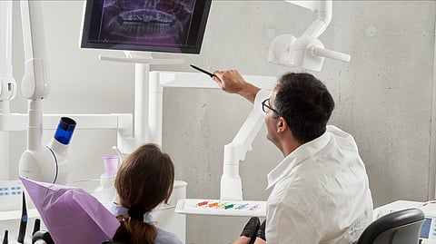 A dentist is explaining some radiographic findings to a patient in a dental chair.