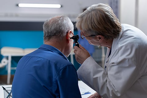 Woman doctor holding otoscope to do ear consultation for old man 