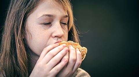 The image depicts a girl eating a burger.