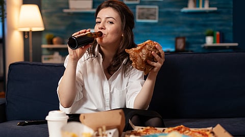 Woman eating junk food and drinking liquor while watching TV.