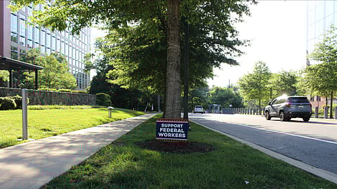A board saying support federal workers placed below a tree on a roadside.