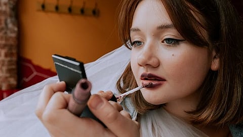 A young woman putting on a dark colored lipstick.