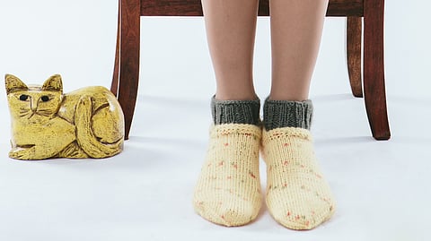 Image shows the feet of a person sitting on a chair wearing beige colored knitted socks.