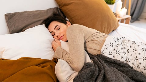 A woman sleeping cozily in the bed with pillows and blankets.