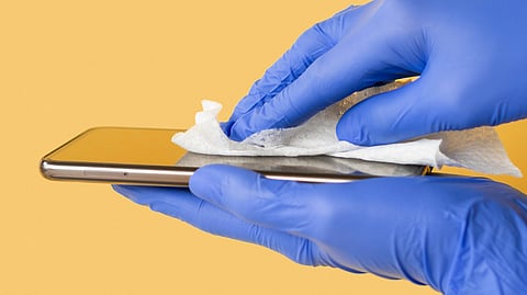 Image of blue-gloved hands cleaning a phone with the help of a wet wipe.