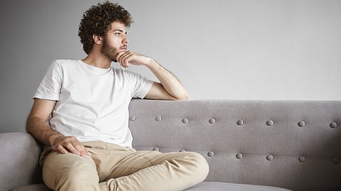 Image shows man sitting with hand on chin, appearing deep in thought as if his brain engaged in daydreaming.