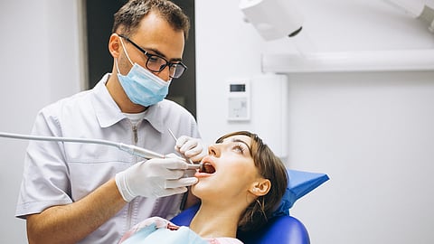 A patient sitting on a dental chair and a dentist checking her oral cavity.