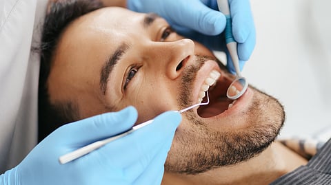 Image depicting man getting dental checkup with tools in his mouth.
