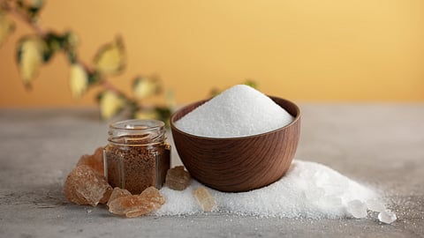 White sugar crystals kept in a wooden bowl and large brown cubes kept nearby.