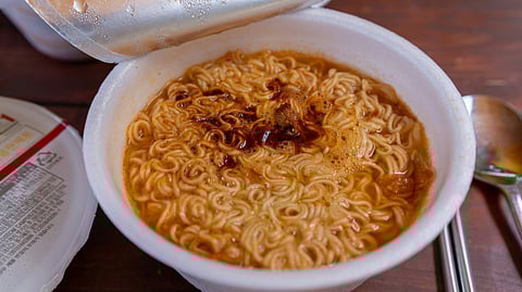 Open cup of noodles showing broth and noodles inside.