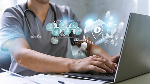 Medical professional working on a computer at a hospital desk wearing a stethoscope.