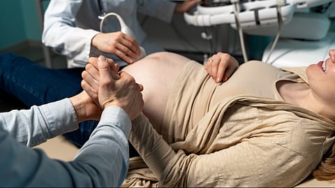 Gynecologist performing ultrasound on woman laying on table while she's holding her husband's hand.