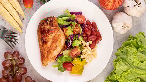Image shows a white bowl filled with chicken, vegetables, nuts, indicating a high- protein meal.