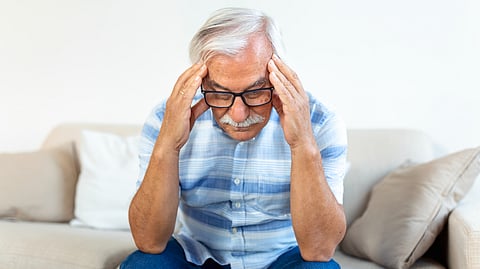 Image shows elderly man holding his head in stress.
