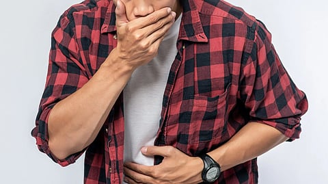 A young man holding his mouth and stomach as he's feeling urge to throw up.