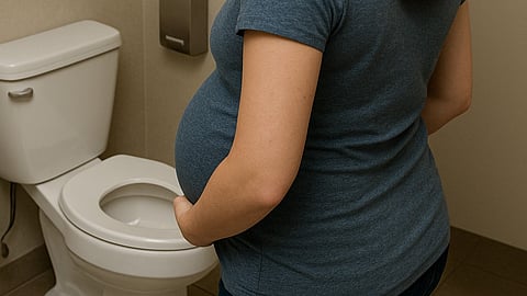 Image shows pregnant woman standing near a toilet in a bathroom.