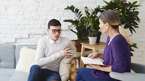 Image shows a man and woman seated on different couch, engaged in conversation about reshaping addiction treatment.