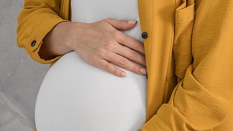 Side view of pregnant woman holding her belly wearing a yellow shirt and a white t-shirt.