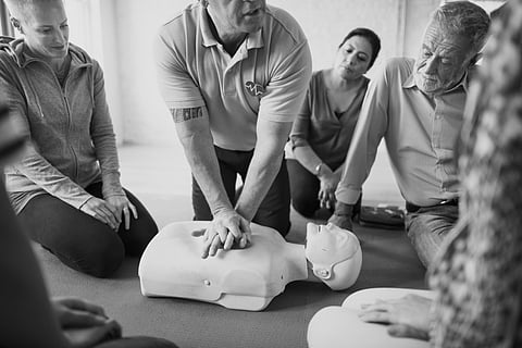 Black and white image of group of people from diverse medical background in a CPR training class.
