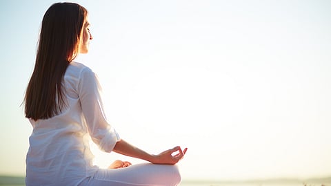 Image shows woman doing meditation in sunlight.