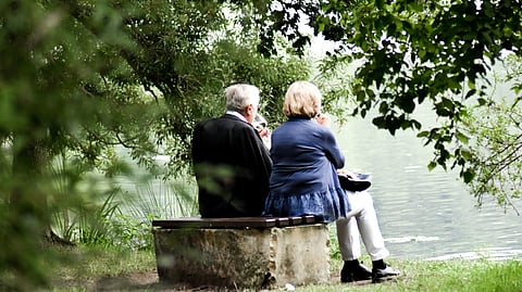 An old couple sitting on a cement bench looking at a river.