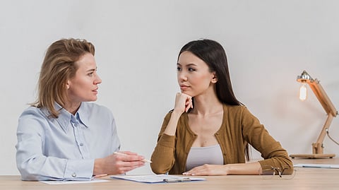 Two women sitting at a desk engaged in a thoughtful conversation.
