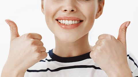 Smiling young woman giving thumbs up with both hands, showing approval and happiness.