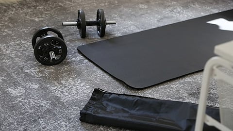 A black yoga mat and a pair of dumb bells on the floor.